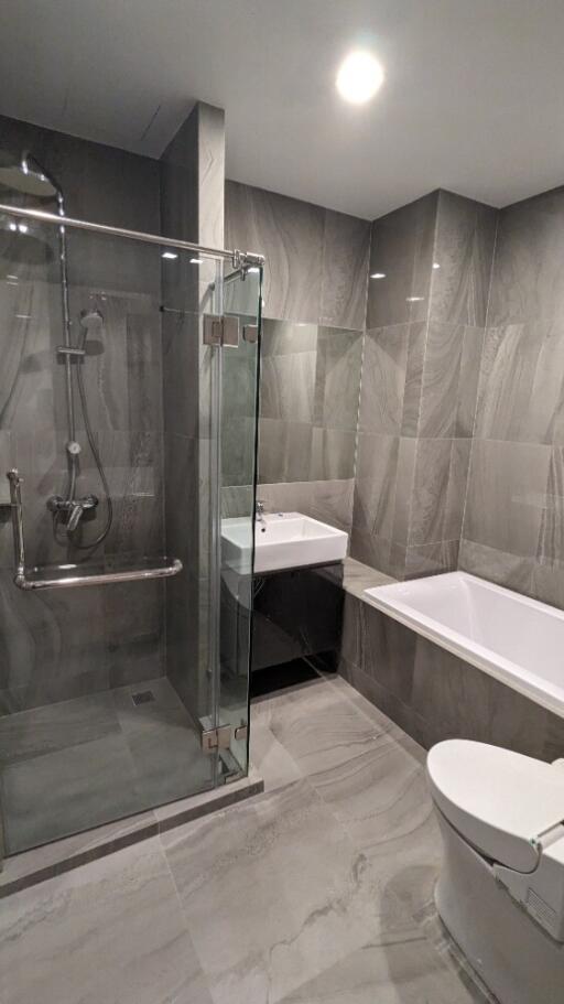 Modern bathroom with glass shower, bathtub, sink, and toilet