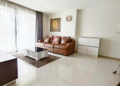 Modern living room with a leather sofa, coffee table, TV, and large windows with sheer curtains