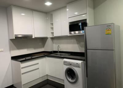 Modern kitchen with white cabinets, appliances including refrigerator, microwave, oven, washing machine, and in-counter stove.