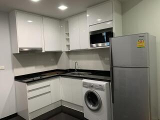 Modern kitchen with white cabinets, appliances including refrigerator, microwave, oven, washing machine, and in-counter stove.