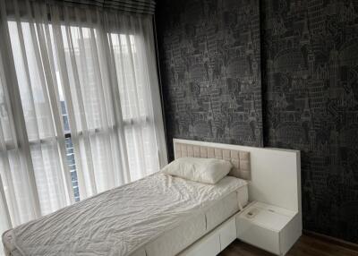 Bedroom with a bed next to large windows with sheer curtains and patterned dark wallpaper