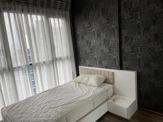 Bedroom with a bed next to large windows with sheer curtains and patterned dark wallpaper