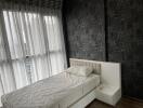 Bedroom with a bed next to large windows with sheer curtains and patterned dark wallpaper