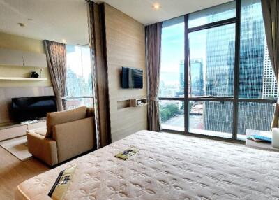 Spacious bedroom with a bed, couch, TV, shelves, and large windows with city view