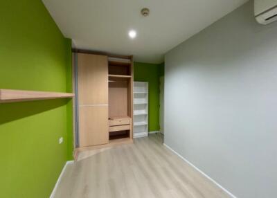 Empty bedroom with green accent wall, integrated wooden wardrobe, and shelf unit.