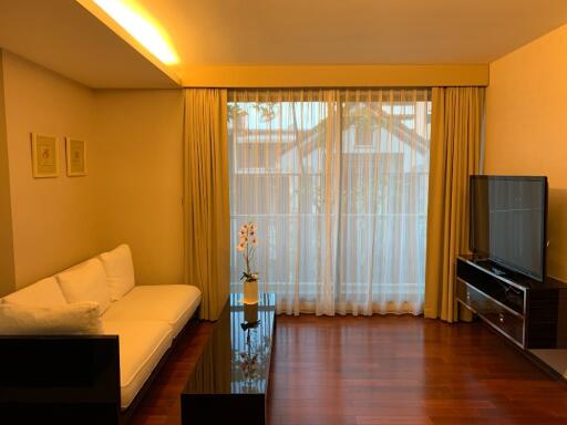 Modern living room with a sofa, coffee table, television, and large window with curtains