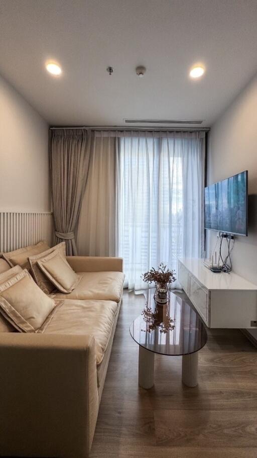 Modern living room with beige sofa, wall-mounted TV, coffee table and sheer curtains