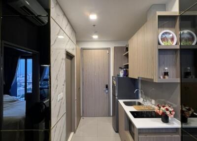 Modern kitchen with beige and wooden tones, featuring appliances and storage, adjacent to a bedroom