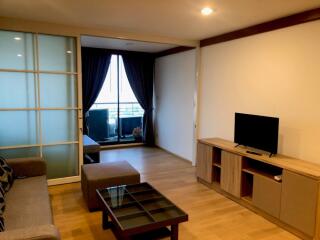 Modern living room with a TV, glass coffee table, and access to a balcony