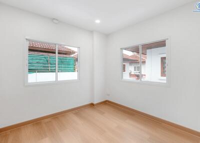 Bright and empty bedroom with two windows and wooden flooring