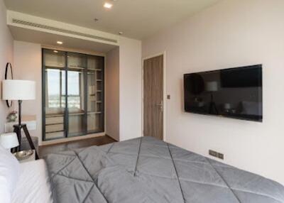 Modern bedroom with a large bed, wall-mounted TV, and a view through a glass door closet.