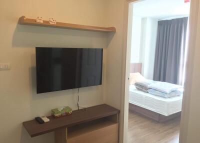 A living room with a wall-mounted TV and a view into the bedroom