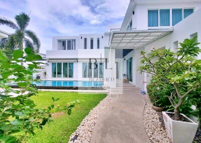 Modern white two-story house with large windows, garden, and pool