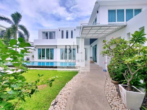 Modern white two-story house with large windows, garden, and pool