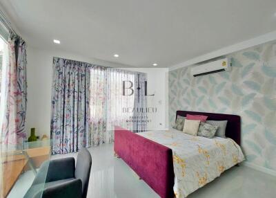 Modern bedroom with floral-patterned curtains and wallpaper, featuring a maroon velvet bed, glass desk, and air conditioning unit