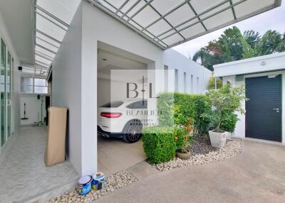 Covered carport with a white car, adjacent storage space, and surrounding greenery