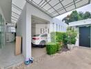 Covered carport with a white car, adjacent storage space, and surrounding greenery