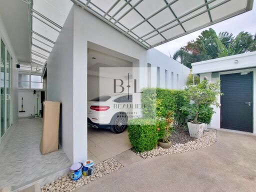 Covered carport with a white car, adjacent storage space, and surrounding greenery