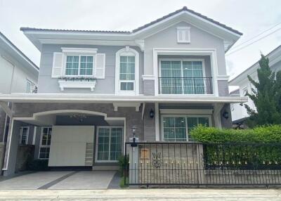 Front view of a two-story grey house with white accents, a small garden, garage, and balcony