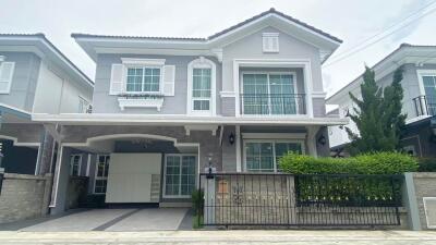 Front view of a two-story grey house with white accents, a small garden, garage, and balcony