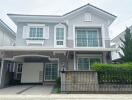 Front view of a two-story grey house with white accents, a small garden, garage, and balcony