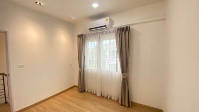 Modern bedroom with wooden flooring and large window with curtains