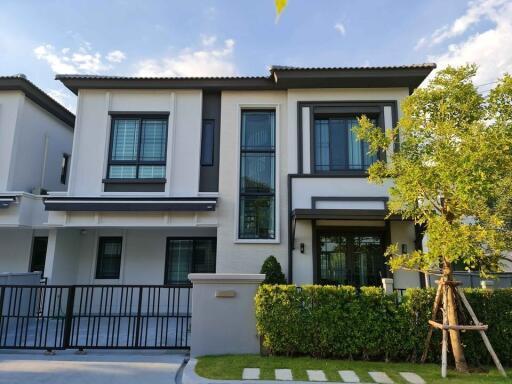 Exterior view of a modern two-story house with large windows and a fenced lawn