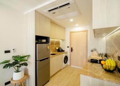 Modern kitchen with light wood cabinetry, appliances, and marble countertops