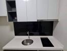 Compact modern kitchenette with white cabinets and black backsplash