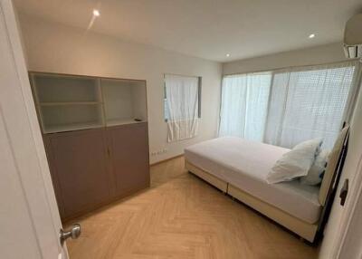 A well-lit bedroom with a large window and furnished with a double bed and a storage cabinet