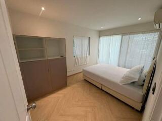 A well-lit bedroom with a large window and furnished with a double bed and a storage cabinet