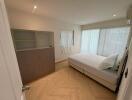 A well-lit bedroom with a large window and furnished with a double bed and a storage cabinet