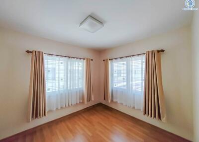 Bright, unfurnished bedroom with wooden floor and double windows with curtains