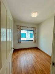 Empty bedroom with wooden flooring, curtained window, and ceiling light