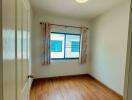 Empty bedroom with wooden flooring, curtained window, and ceiling light