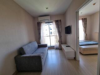 Modern living room with grey sofa, flat-screen TV, and access to bedroom