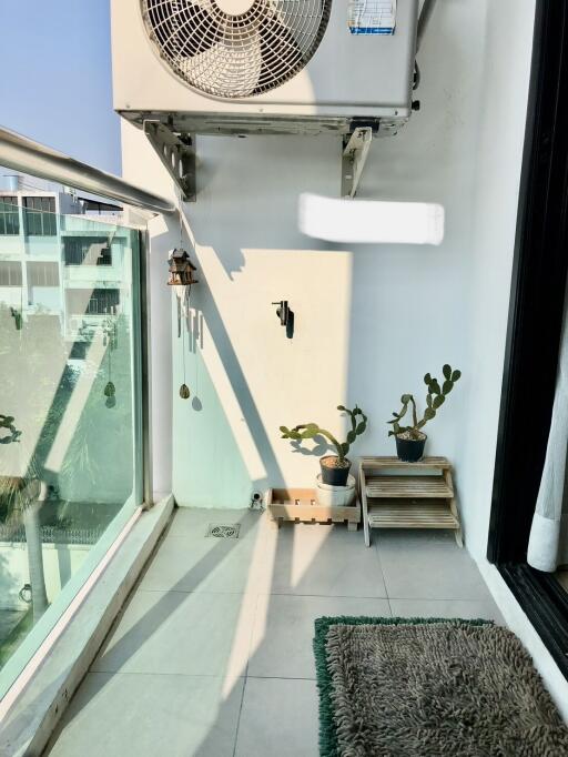 Modern balcony with glass railing, potted plants, and an AC unit