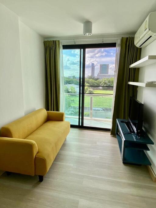 Bright living room with a large window, green view, yellow couch, and TV