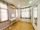 image of a bedroom with wooden flooring, a vanity table, air conditioning, and large windows with curtains