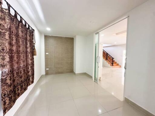 Spacious living room with tiled floor and decorative curtains, connected to a staircase