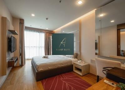 Modern bedroom with wooden flooring, large window, bed, wall-mounted TV, and desk.