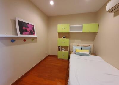 A cozy bedroom with wooden flooring, single bed, wall-mounted storage, and minimal decor.