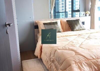 Modern bedroom with a neatly made bed, large windows, and decorative pillows.