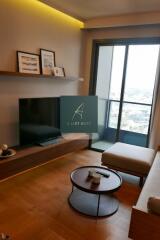 Modern living room with a balcony, featuring a wall-mounted TV, a chaise lounge, and decorative items on a shelf.