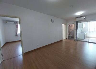 Spacious empty living room with wooden floor and view into kitchen and other rooms