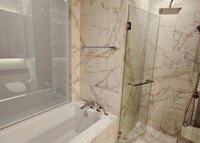 Modern bathroom with marble tiles, bathtub, and glass shower enclosure.