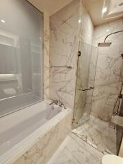 Modern bathroom with marble tiles, bathtub, and glass shower enclosure.