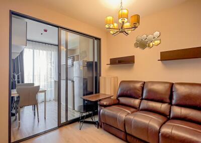 Living room with brown leather sofa, light wood flooring, and sliding glass door to dining area