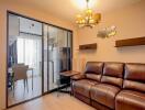 Living room with brown leather sofa, light wood flooring, and sliding glass door to dining area