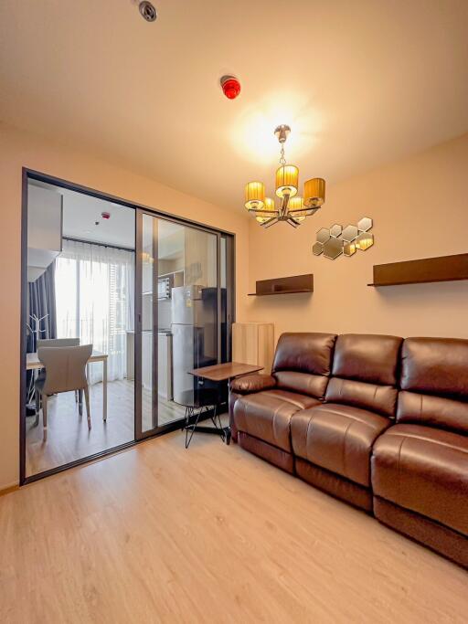 Living room with brown leather sofa, light wood flooring, and sliding glass door to dining area